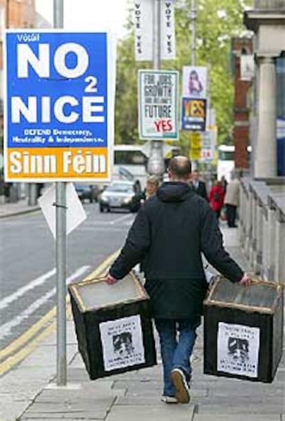 Un hombre con dos urnas pasa junto a un cartel que pide el <b></b><i>no</i> en Dublín.