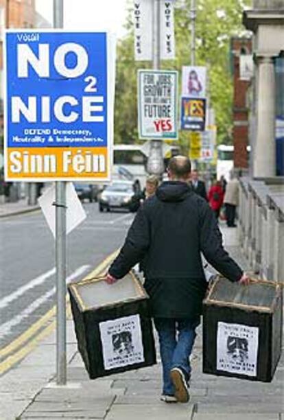 Un hombre con dos urnas pasa junto a un cartel que pide el <b></b><i>no</i> en Dublín.