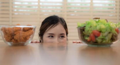 Una mujer observa una ensalada de verduras y un plato con pollo frito.