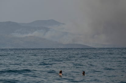 Unos bañistas nadan cerca de la ciudad costera de Saranda mientras el humo se extiende en la isla griega de Corfú.