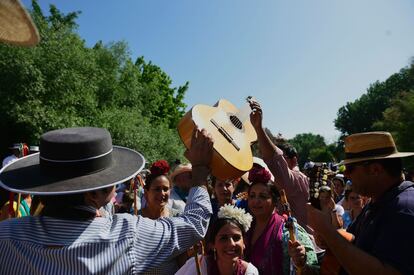 Dos romeros se pasan una guitarra durante la procesión a su paso por el río Quema.