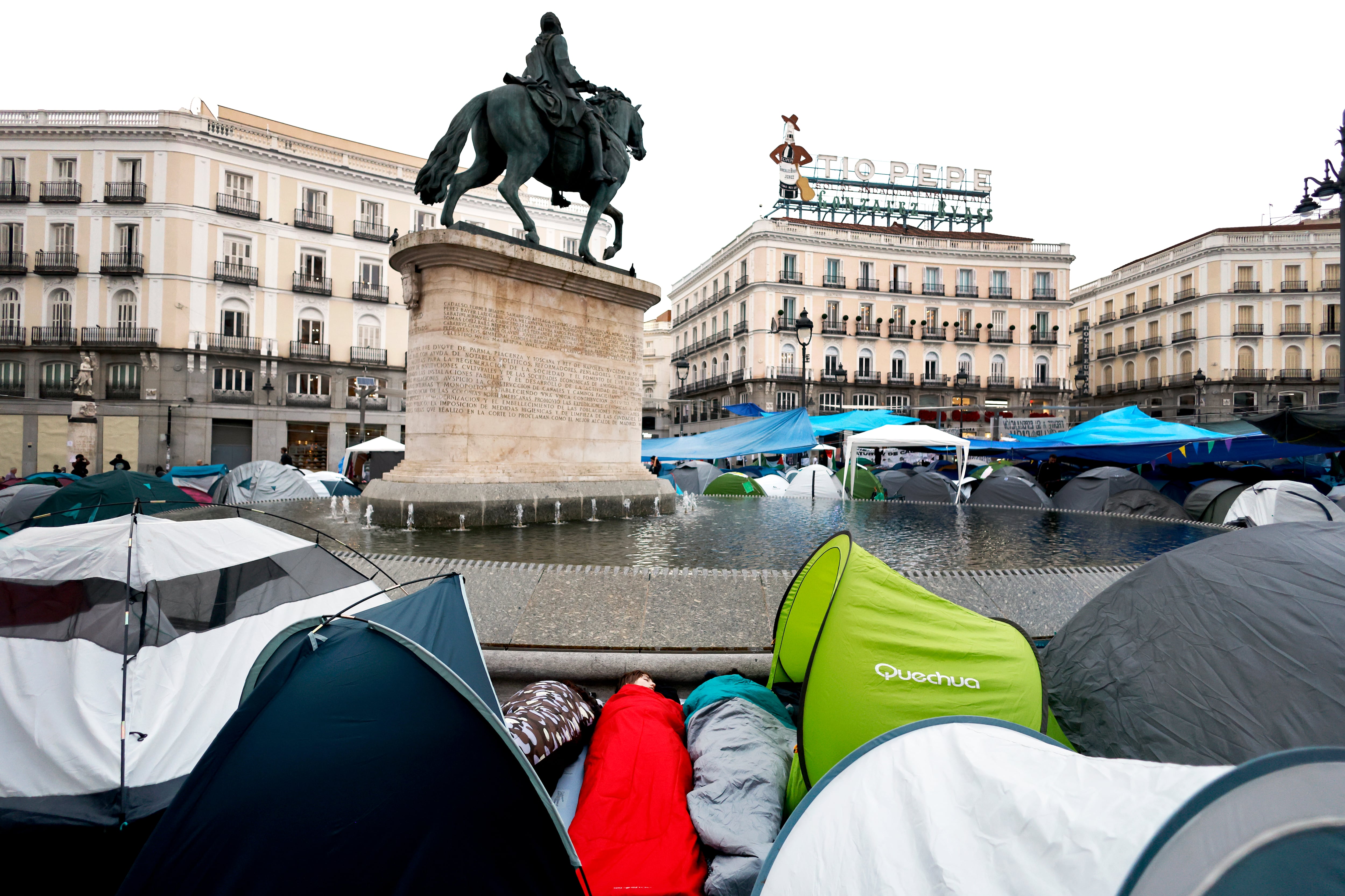 Dos jóvenes duermen entre tiendas de campana en la Puerta del Sol de Madrid, este lunes. 