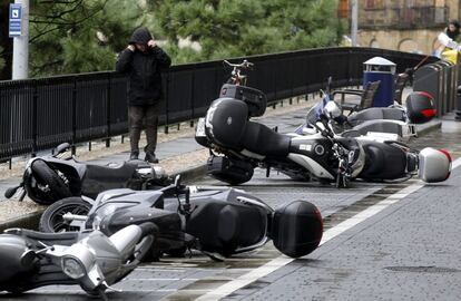 Un hombre pasa junto a varias motos derribadas por las fuertes rachas de viento que se registran en la capital donostiarra.