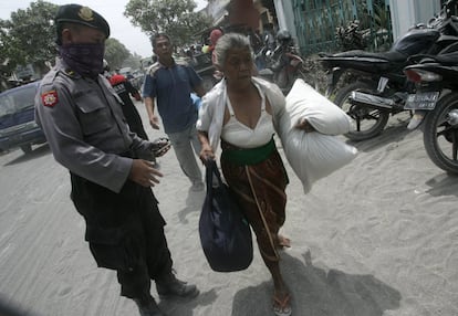 Un policía da indicaciones a una mujer que carga con alguna de sus pertenencias tras abandonar su casa por la erupción del volcán Kelud en Kediri, Java Oriental (Indonesia), 14 de febrero de 2014.