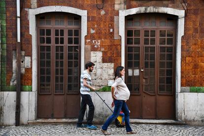 Una pareja pasea por el centro de Lisboa, delante de una casa donde han sido robados o desprendidos varios azulejos.