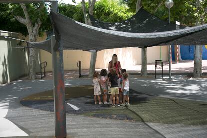 Una profesora juega con varios alumnos de infantil en el patio del CEIP Guindalera, en Madrid, bajo un toldo comprado por los padres. 