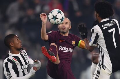 El jugador del Barcelona, Andrés Iniesta, lucha un balón con los jugadores de la Juventus Douglas Costa y Juan Cuadrado.