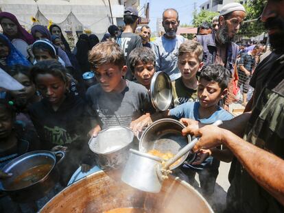 Varios niños palestinos desplazados reciben comida caliente distribuida por una ONG, este miércoles en Deir Al-Balah en Gaza.