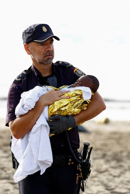 Un policía lleva en brazos al bebé de tres meses que viajaba en el cayuco.