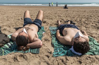 Dos bañistas en la playa de la Malvarrosa (Valencia) toman el sol con mascarilla.