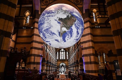 Visitantes de la catedral de San Pablo, en Melbourne, observan la obra 'Gaia', del artista Luke Jerram, un globo terráqueo gigante de siete metros de diámetro suspendido en el techo, donde rota.