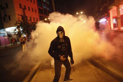 Un manifestante con una máscara antigas se aleja del impacto de una granada de gas lacrimógeno lanzada por la policía.