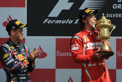 Alonso besa el trofeo que le acredita como ganardor del Gran Premio de Silverston en presencia del actual líder del Mundial, Sebastien Vettel, que ha quedado segundo