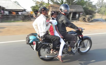 Tres personas, dos de ellas sin casco, en moto por una carretera de India.
