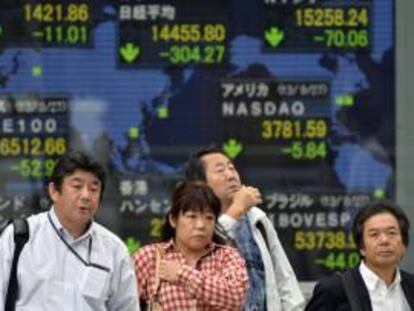 Unos ciudadanos pasan por delante de una pantalla con los resultados de la bolsa de Tokio. EFE/Archivo