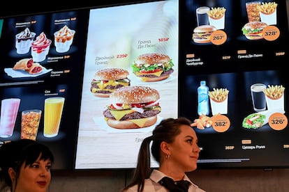 Two employees in front of a sign displaying the chain’s products. 