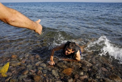 Um grego ajuda um refugiado sírio que chega exausto à costa da ilha grega de Lesbos.