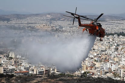 Un helicóptero vierte agua sobre una colina afectada por un incendio en el barrio de Vironas (Atenas).