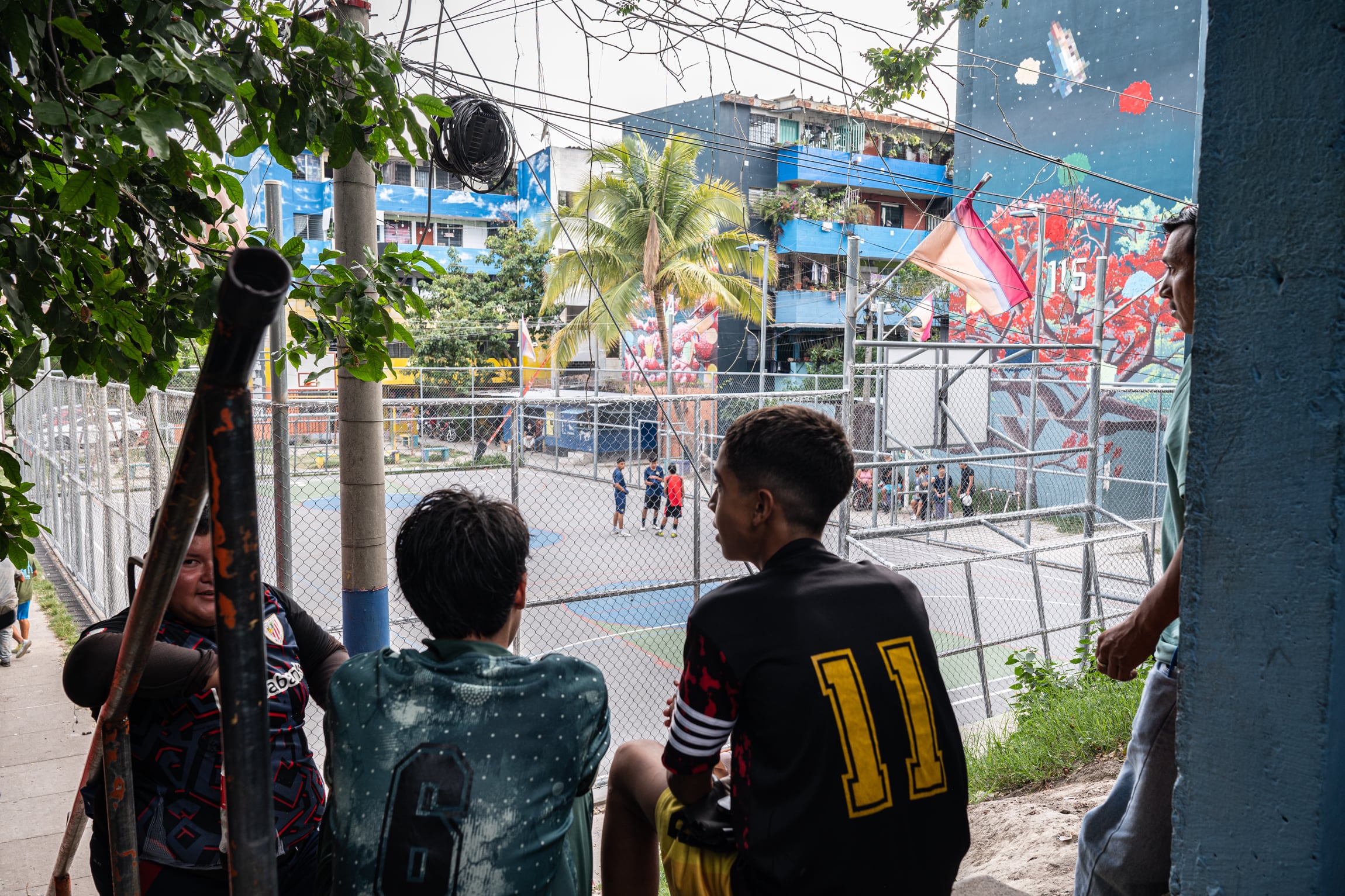 Unos jóvenes charlan cerca de la cancha de Zacamil a primera hora de la tarde. Durante la época en que las bandas controlaban la zona, era imposible circular por la colonia durante la noche. Fotografía tomada en San Salvador, el 25 de abril de 2026.