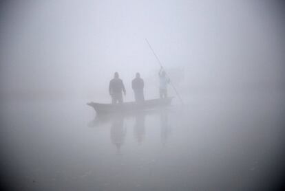 Gente en un bote alcanzando la orilla del río Rapti durante un mañana con una densa niebla en Sauraha (Nepal).
