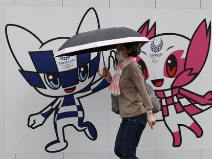 Una mujer pasea por Tokio ante una valla con las mascotas olímpicas.