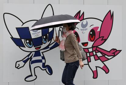 Una mujer pasea por Tokio ante una valla con las mascotas olímpicas.