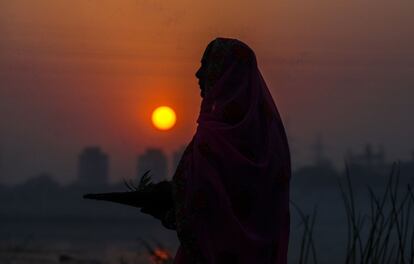 Uma mulher indiana realiza rituais para venerar o pôr do sol nas águas do rio Sabarmati, em Ahmedabad (Índia).