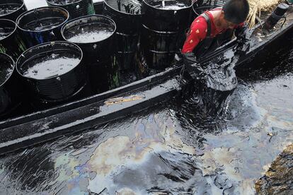 Un operario retira crudo con sus propias manos para cargarlo en bidones en el puerto de Dalian (AFP PHOTO / GREENPEACE / HO / JIANG HE).