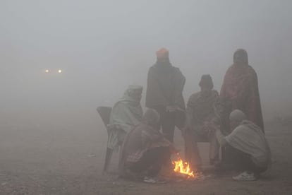 Trabajadores indios se sientan alrededor de una hoguera para calentarse en una fría mañana de niebla en un mercado de verduras al por mayor en las afueras de Amritsar (India).