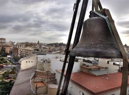 Momento en que la grúa izaba, ayer, sobre el perfil de los tejados de Valencia, la campana mayor de la iglesia de San Martín, que será restaurada.