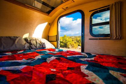 Cama dentro de una caravana ubicada en plena naturaleza.