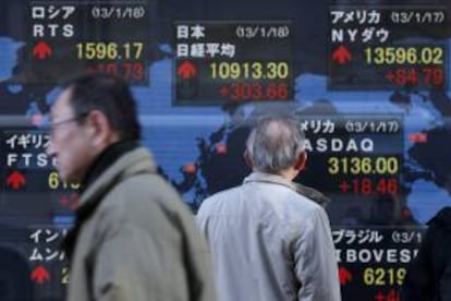 Varios hombres caminan junto a un panel electrónico que muestra el selectivo Nikkei en Tokio. EFE/Archivo