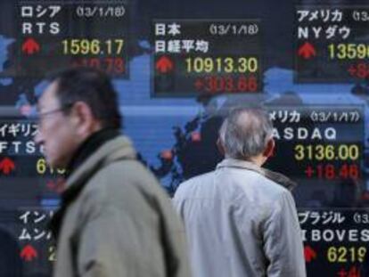 Varios hombres caminan junto a un panel electrónico que muestra el selectivo Nikkei en Tokio. EFE/Archivo