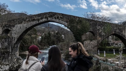 Tres jóvenes miran en sus teléfonos las fotos que se han hecho, en el puente romano de Cangas de Onís.