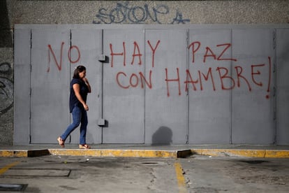 Una mujer camina frente a un muro donde se puede leer una pintada que dice: "No hay paz con hambre".
