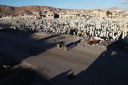 Un hombre pasa en moto por delante de un cementerio, en la ciudad de Duma (Siria).