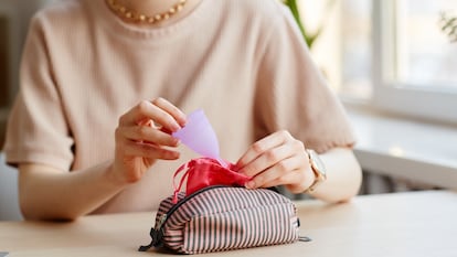 Una mujer guardando una copa menstrual dentro de su bolsa de transporte.