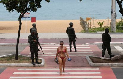 Mulher caminha na orla da praia da Costa em meio aos soldados.