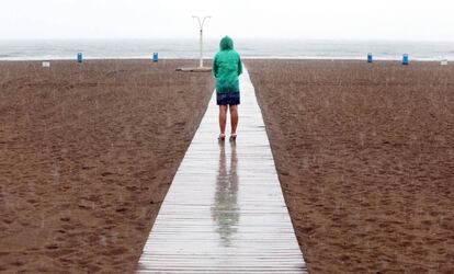 Una mujer contempla la playa de la Malvarrosa bajo la lluvia.