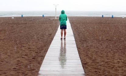 Una mujer contempla la playa de la Malvarrosa bajo la lluvia.