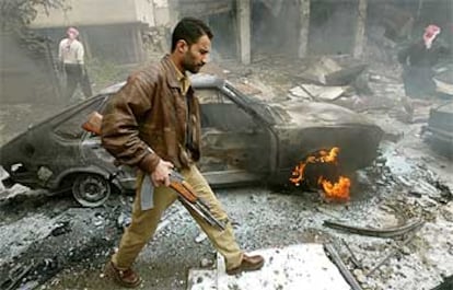 Un iraquí armado pasa delante de un coche ardiendo tras la explosión de dos bombas en un mercado de Bagdad.