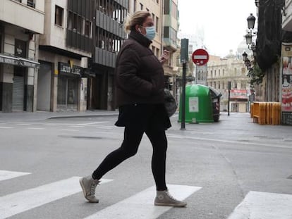 Una mujer protegida con una mascarilla camina por una calle vacía.