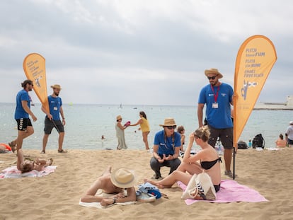 Dos informadores conversan de la nueva prohibición de fumar con bañistas, en la playa del Bogatell, Catalunya (España).