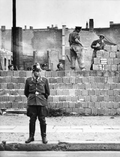 Un policía de Berlín Occidental hace guardia mientras varios albañiles trabajan en el Muro de Berlín.