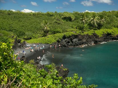 People spend time on the black sand beach at Waianapanapa State Park in Hana, Hawaii