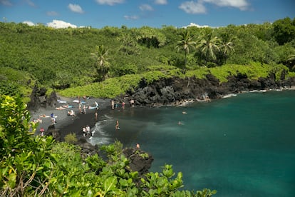 People spend time on the black sand beach at Waianapanapa State Park in Hana, Hawaii