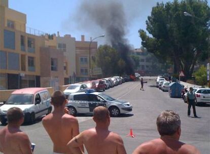 El coche en el que murieron los dos agentes arde tras la explosión mientras lo observan varios turistas.