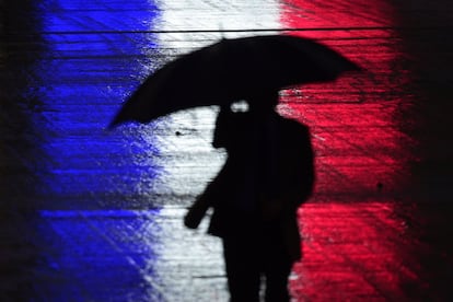 Un hombre con un paraguas ante la luz reflejada con los colores de la bandera de Francia en el estadio Wembley, donde se disputará un partido amistoso entre Inglaterra y Francia.