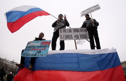 Manifestantes pró-Rússia seguram uma bandeira russa e um cartaz que diz "Nossos irmãos da Rússia, nós somos escravos da Europa" durante ato em frente ao prédio da administração de Donetsk, distrito industrial ucraniano na fronteira com a Rússia.