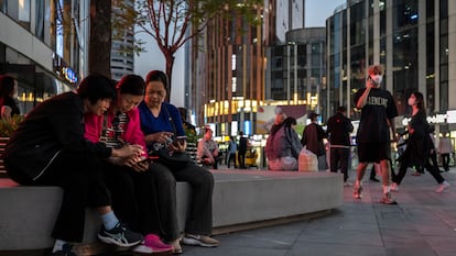 Un grupo de mujeres miran sus móviles en una área central de Pekín, China.
